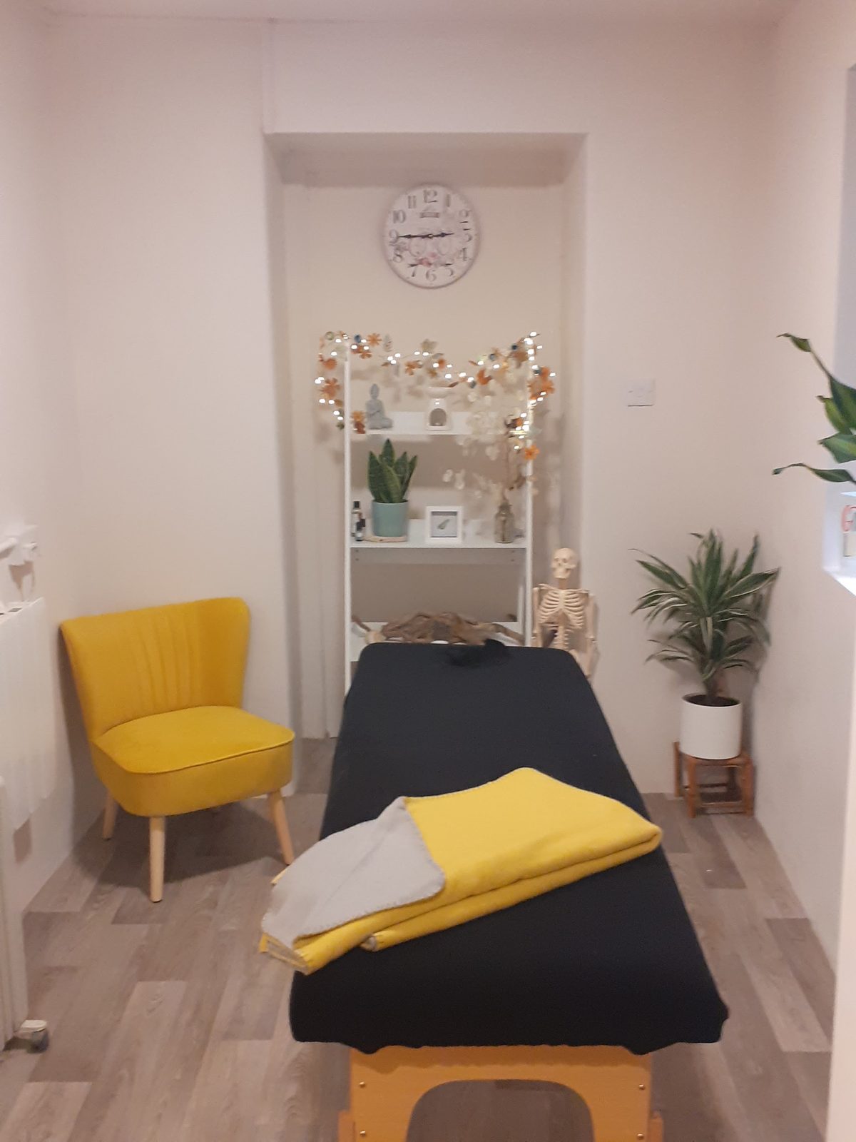 Victoria's treatment room: a massage couch with a yellow towel, a yellow armchair and a shelf of plants and fairy lights